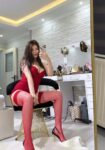 Person in red lingerie and fishnet stockings sits on a gold chair, taking a selfie in a makeup vanity with cosmetics on the desk.